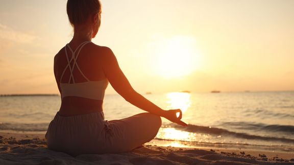 Eine junge Frau macht bei Sonnenuntergang am Strand Yoga. 